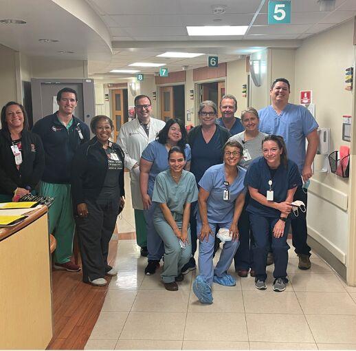 Jackiethia Butsch in scrubs at a hospital, posing with 11 other people who are also wearing scrubs.