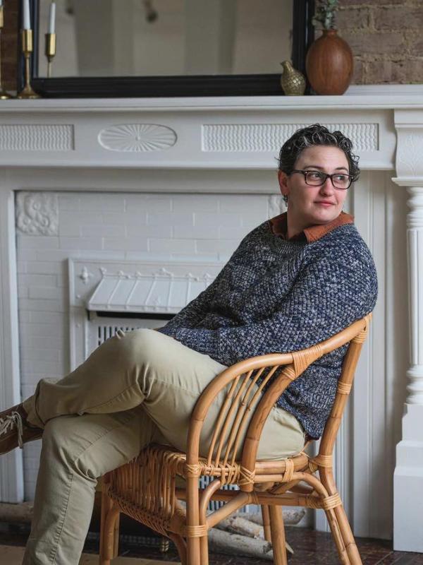 Glennon Sweeney sitting in a wooden chair by a white fireplace.