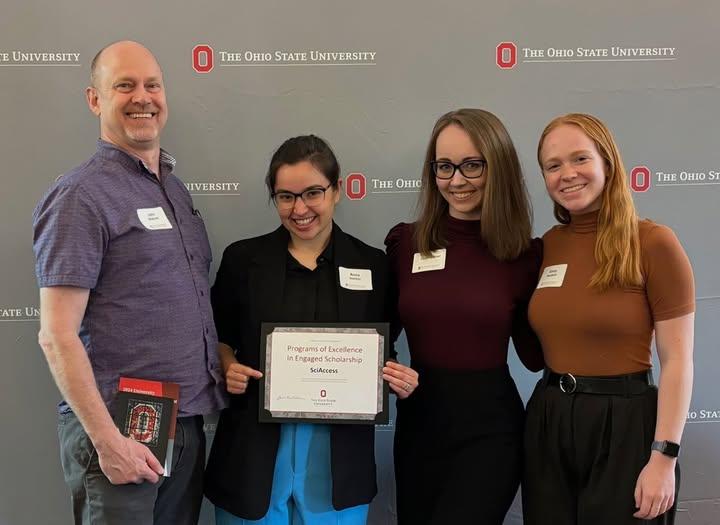 John Beacom with three other people. One person is holding up an award that states "Programs of Excellence in Engaged Scholarship."