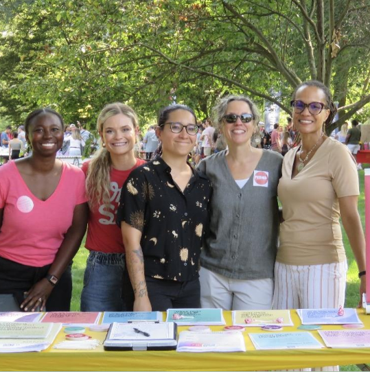Mary Thomas and Tiyi Morris outside at a tabling event with three other people.