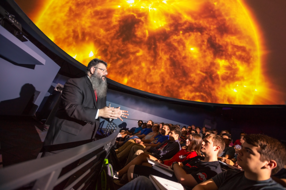 Michael Stamatikos speaking in the SciDome Planetarium in front of a close up of the sun.